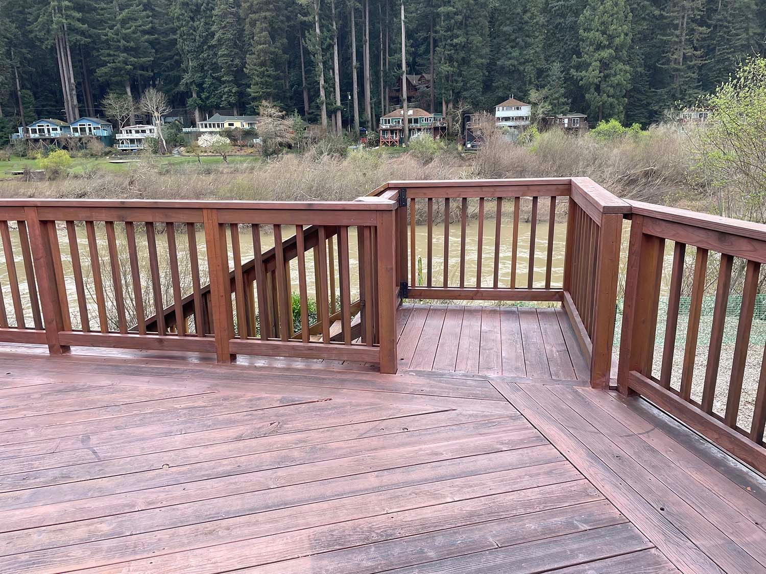 Wooden deck with railings overlooking a forested lakeside area