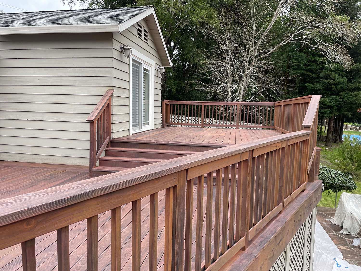 Wooden deck with railings beside a house, extending into a tree-lined yard.