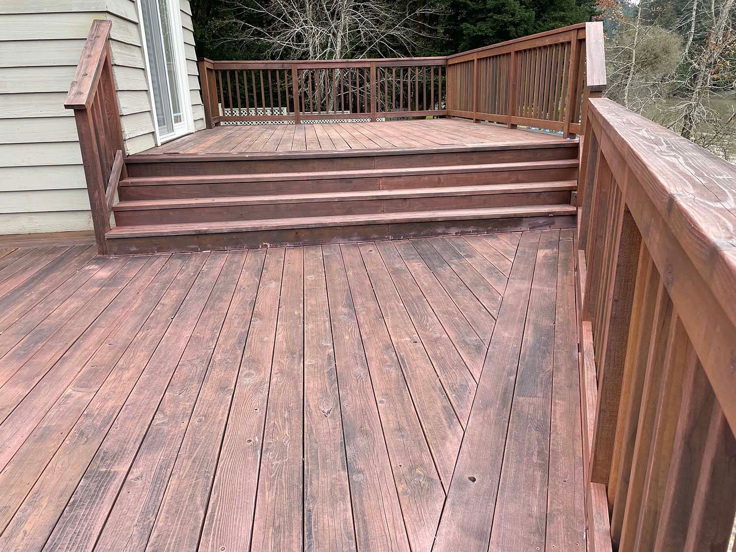 Wooden deck with steps and railings beside a house, leading to an outdoor seating area.