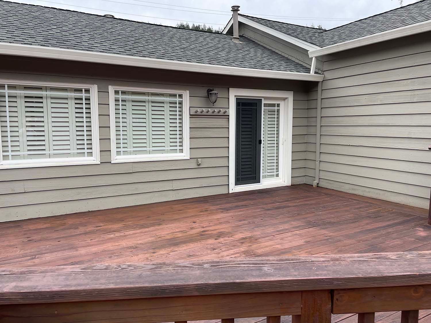 Wooden deck patio with white house siding, shuttered windows, and a glass door.