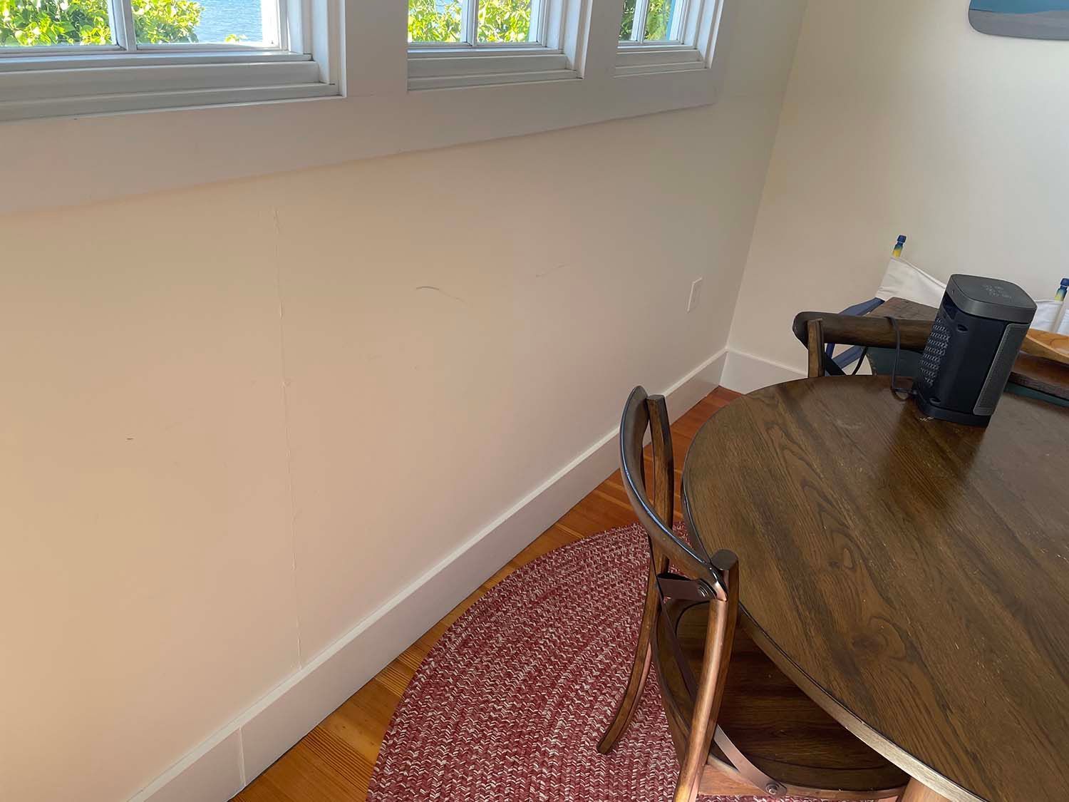 Corner of a dining room with a round wooden table, metal chair, windows, and carpeted floor.