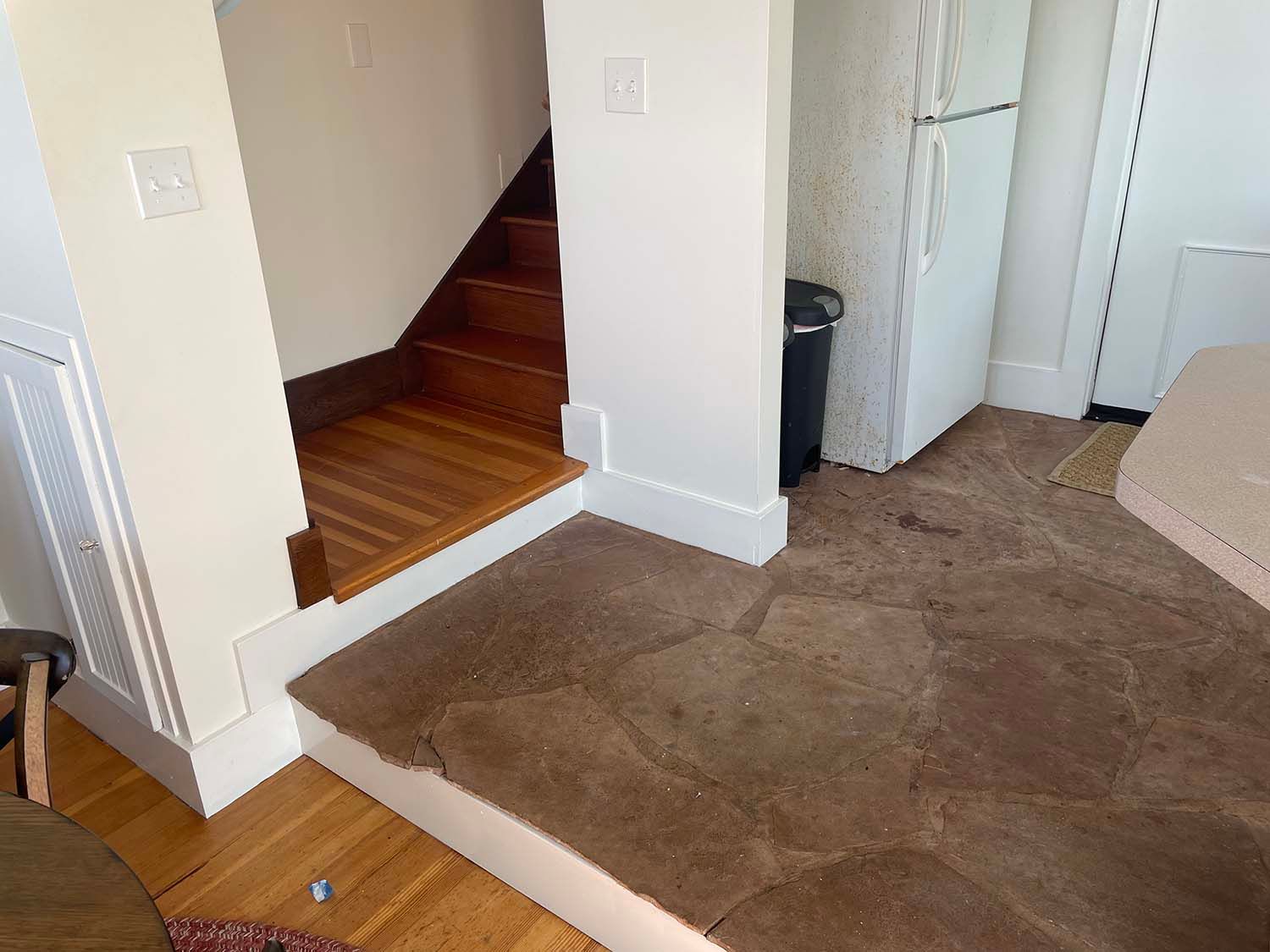Carpeted room with a stairway opening, white walls, and a beige couch on the right.