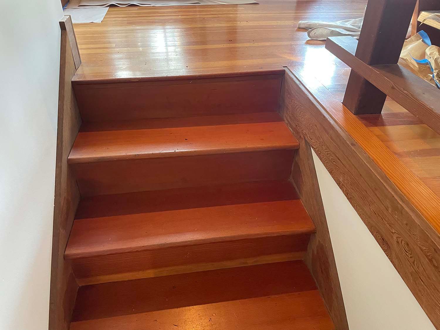 Wooden indoor staircase with three red-brown steps leading to a polished landing.