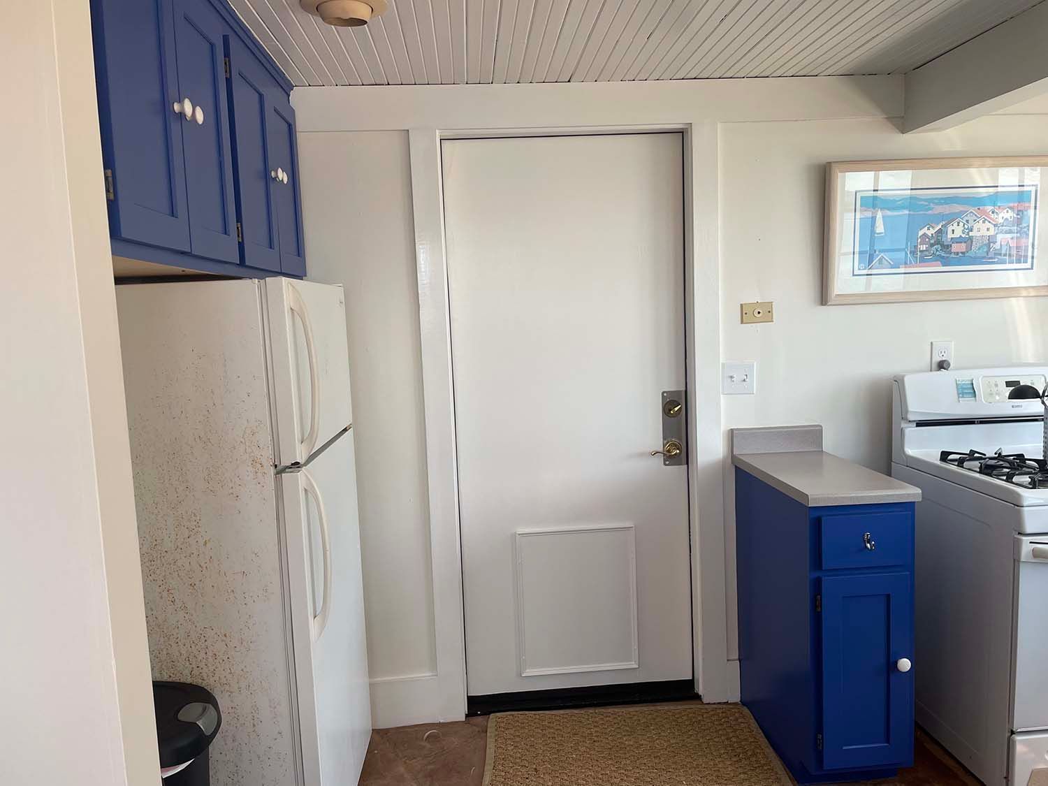 Small kitchen with white fridge, blue cabinets, and a white back door.