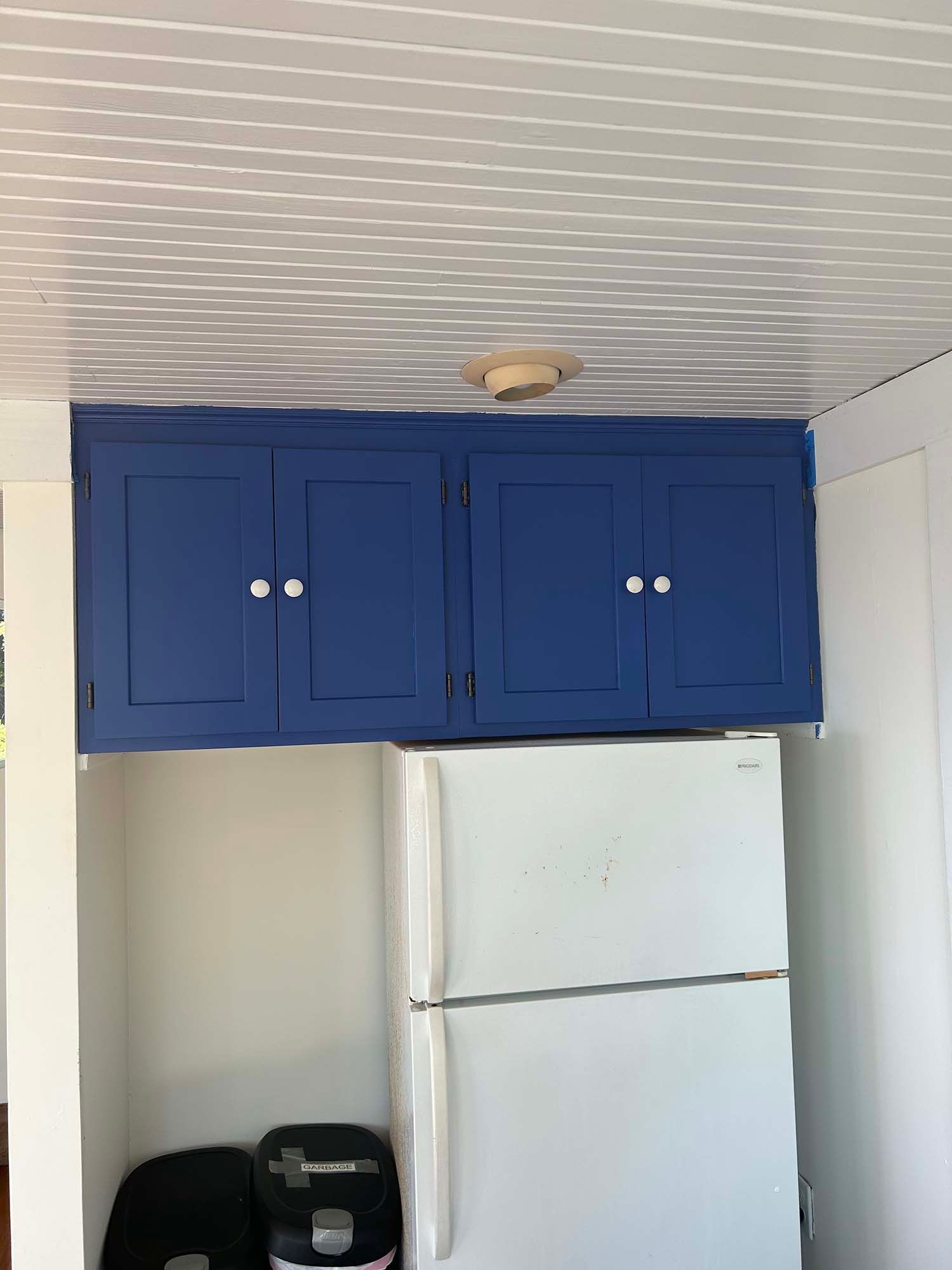 Blue kitchen cabinets above a white refrigerator in a small kitchen.