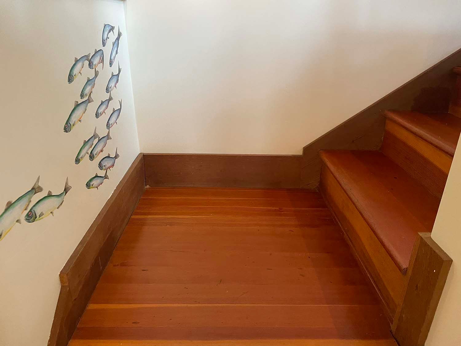 Wooden staircase landing with brown steps and a white wall decorated with fish drawings
