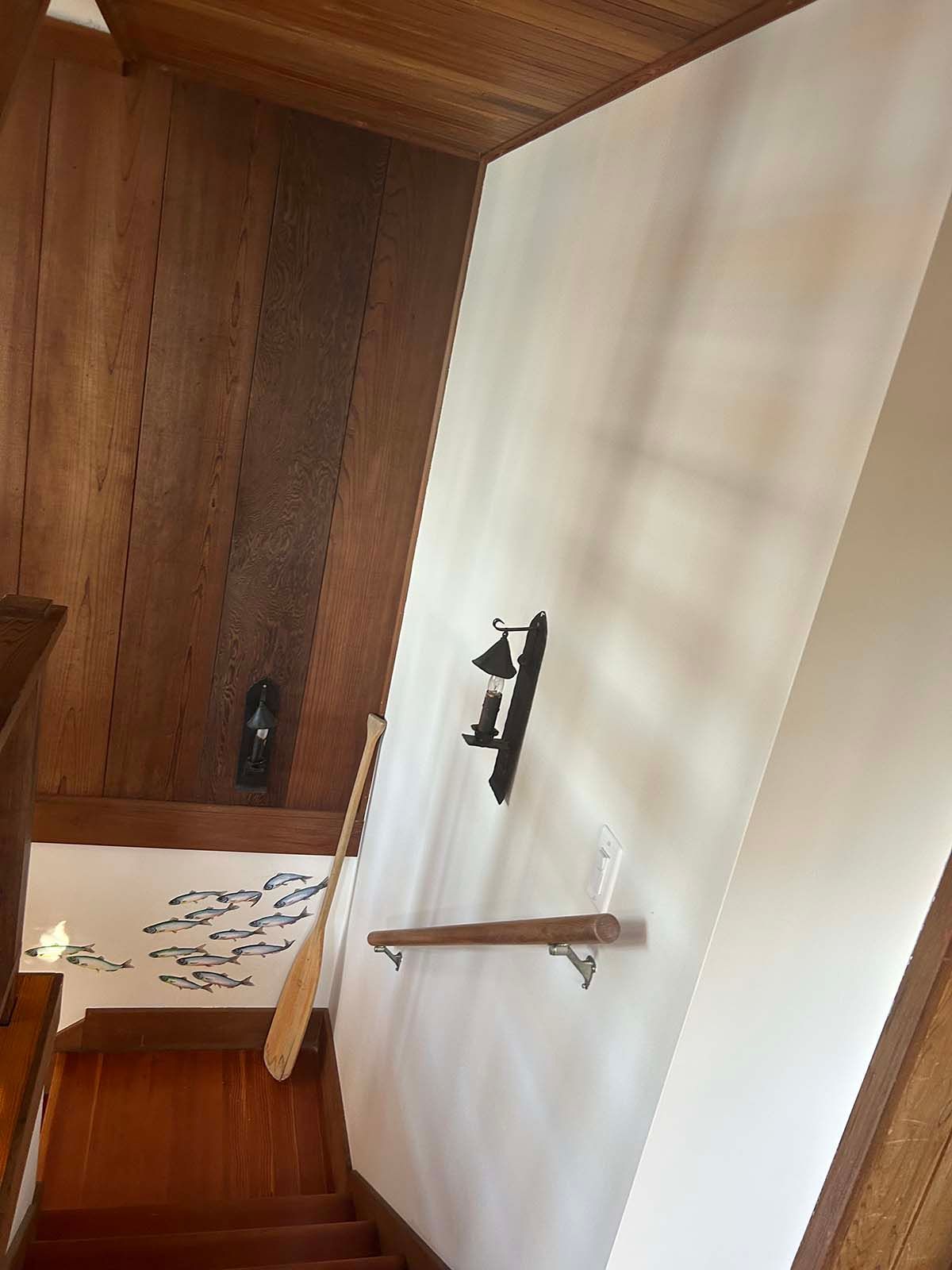 Wood-paneled stairway with white wall, black wall sconce, and a wooden handrail in a home interior