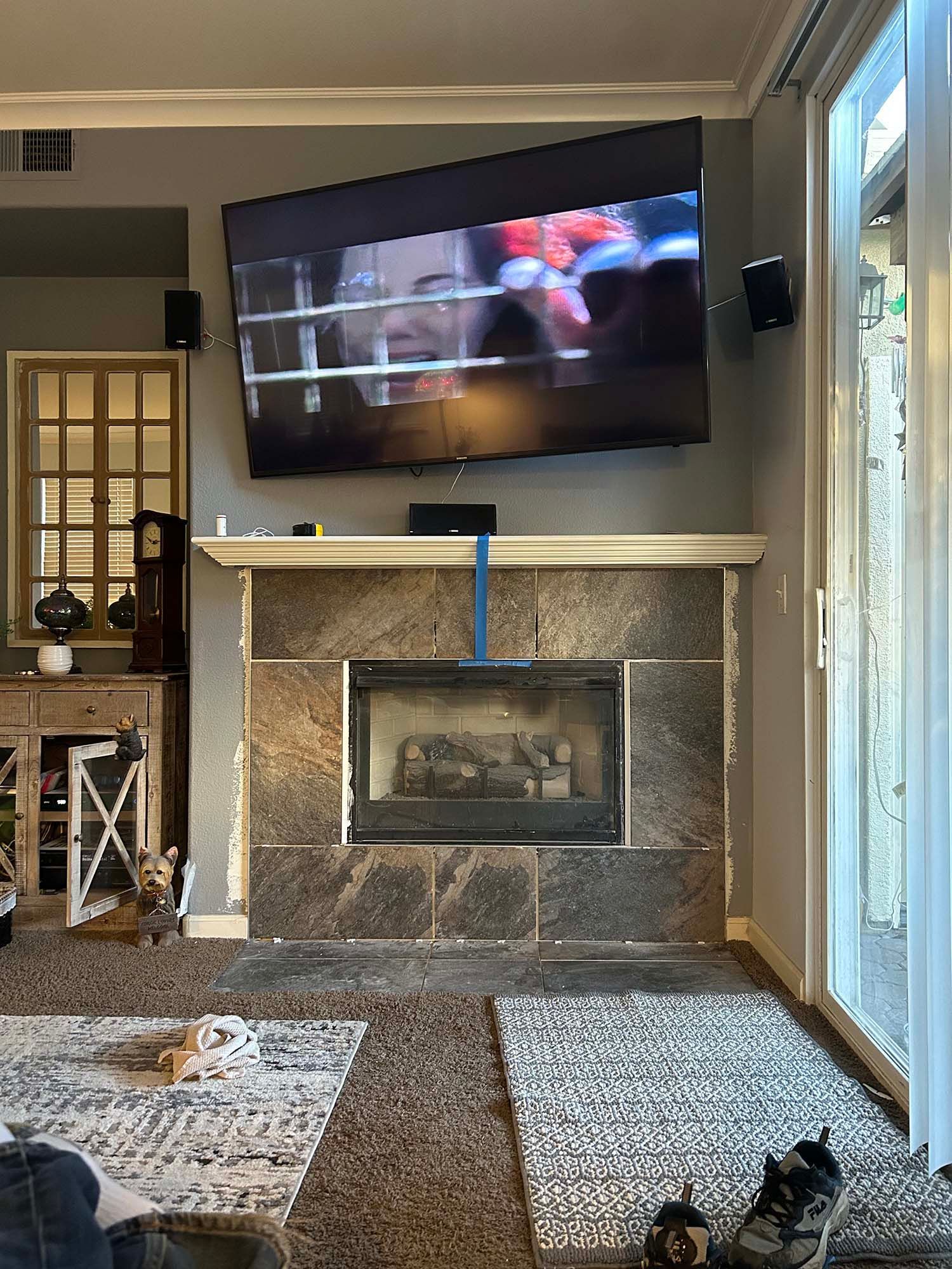 Living room with wall-mounted TV above a fireplace, patterned rug, and a small dog at bottom right