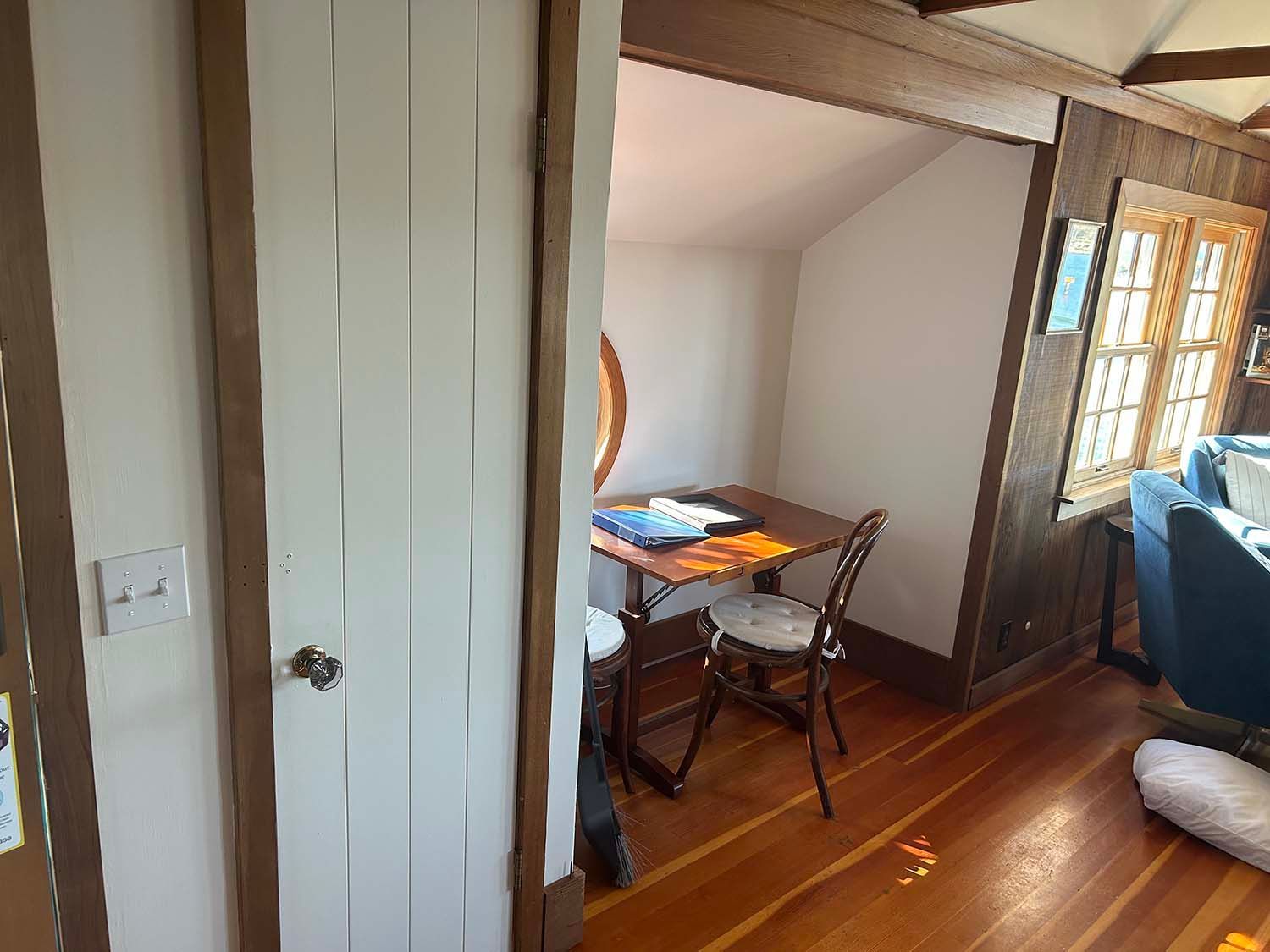 Small dining nook with a table and chairs beside a wooden staircase in a sunlit home.