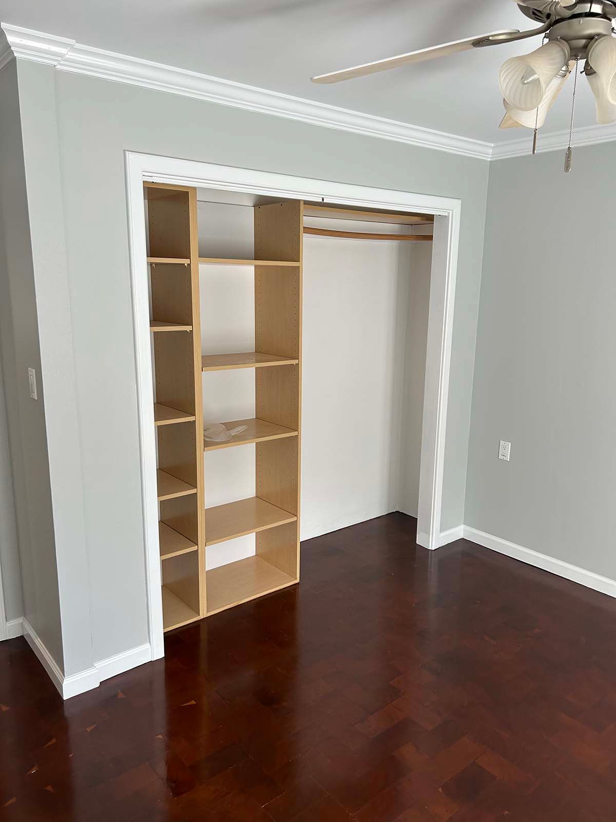 Empty bedroom with open closet shelving and dark hardwood floors