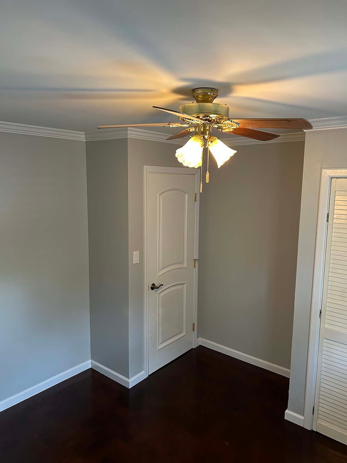 Empty room with dark hardwood floor, gray walls, white doors, and a ceiling fan with lights.