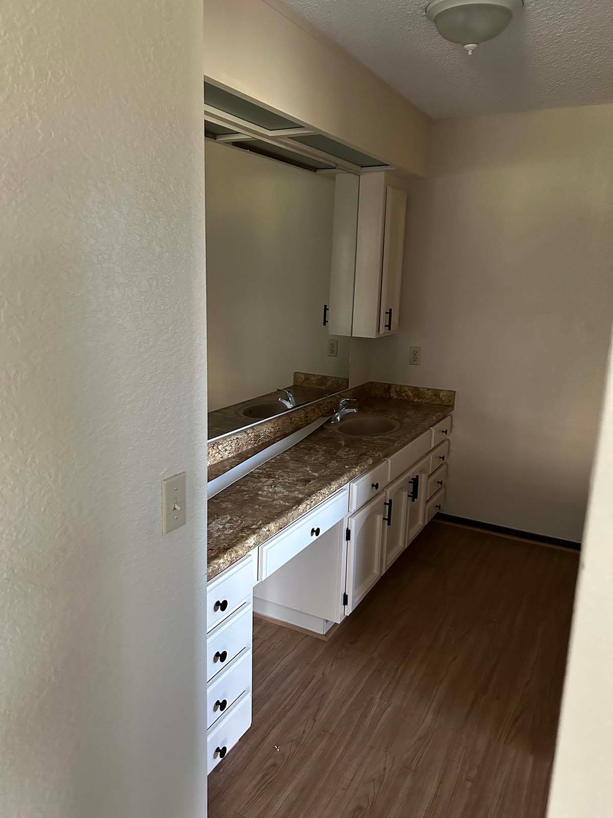 Narrow kitchen with granite counter, white cabinets, wood flooring, and a small window above the sink area