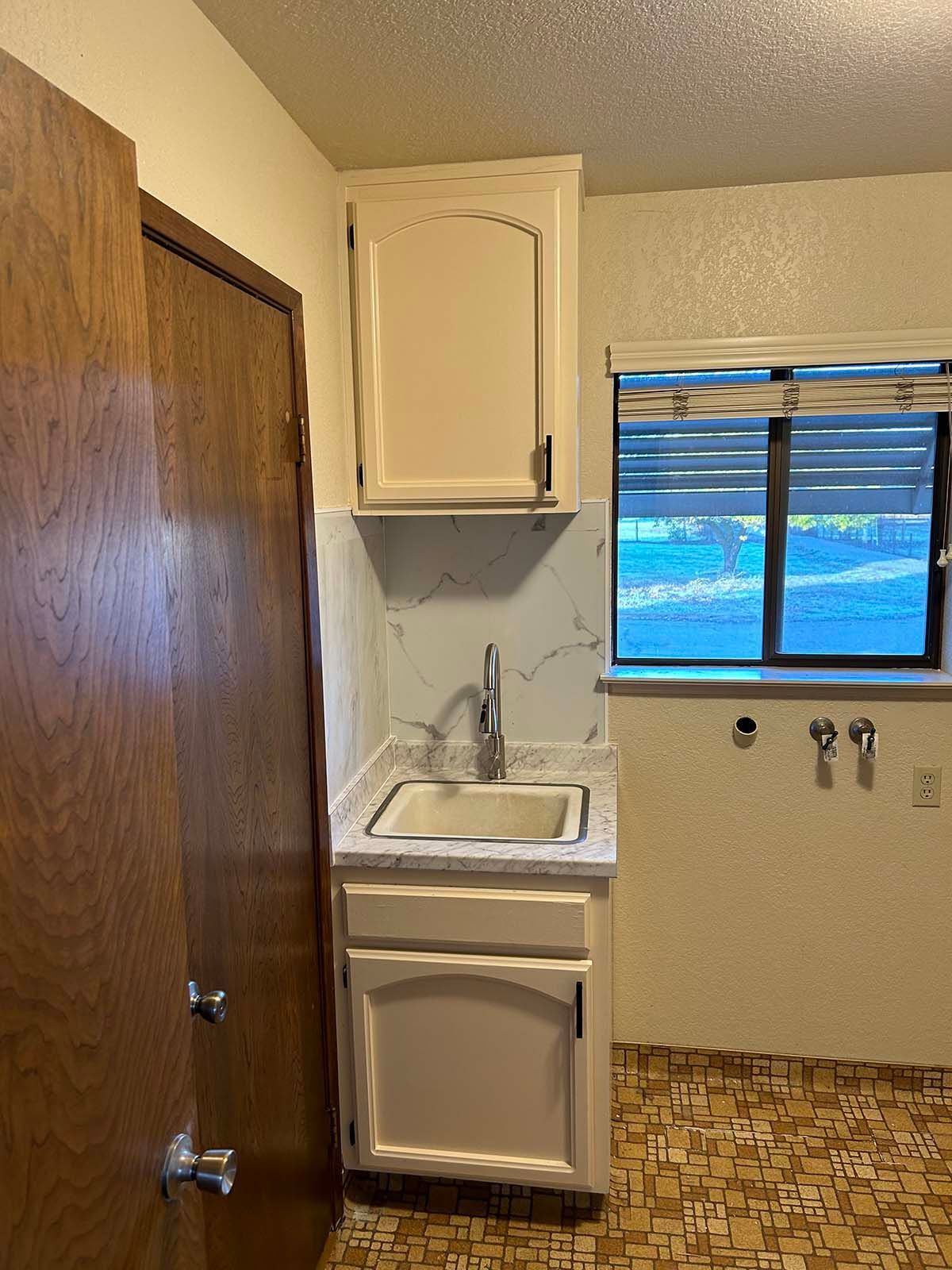 Small kitchen nook with sink, cabinet, and window beside a wooden door