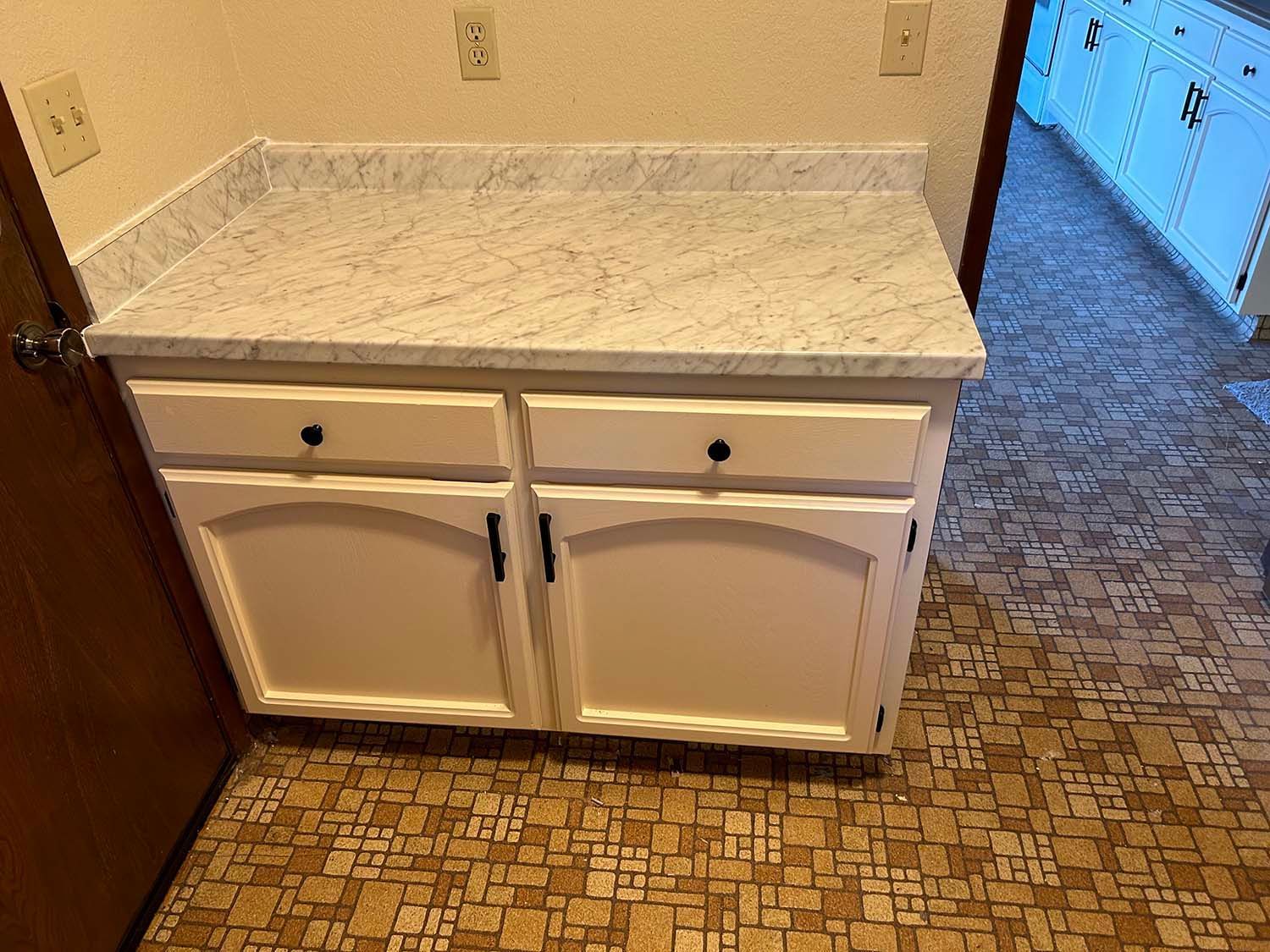 White bathroom vanity with marble countertop and tiled floor against a beige wall.