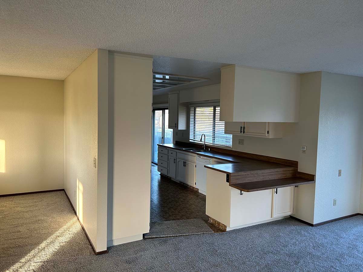 Empty living room with carpet and a kitchen pass-through, beige walls, and wood countertops