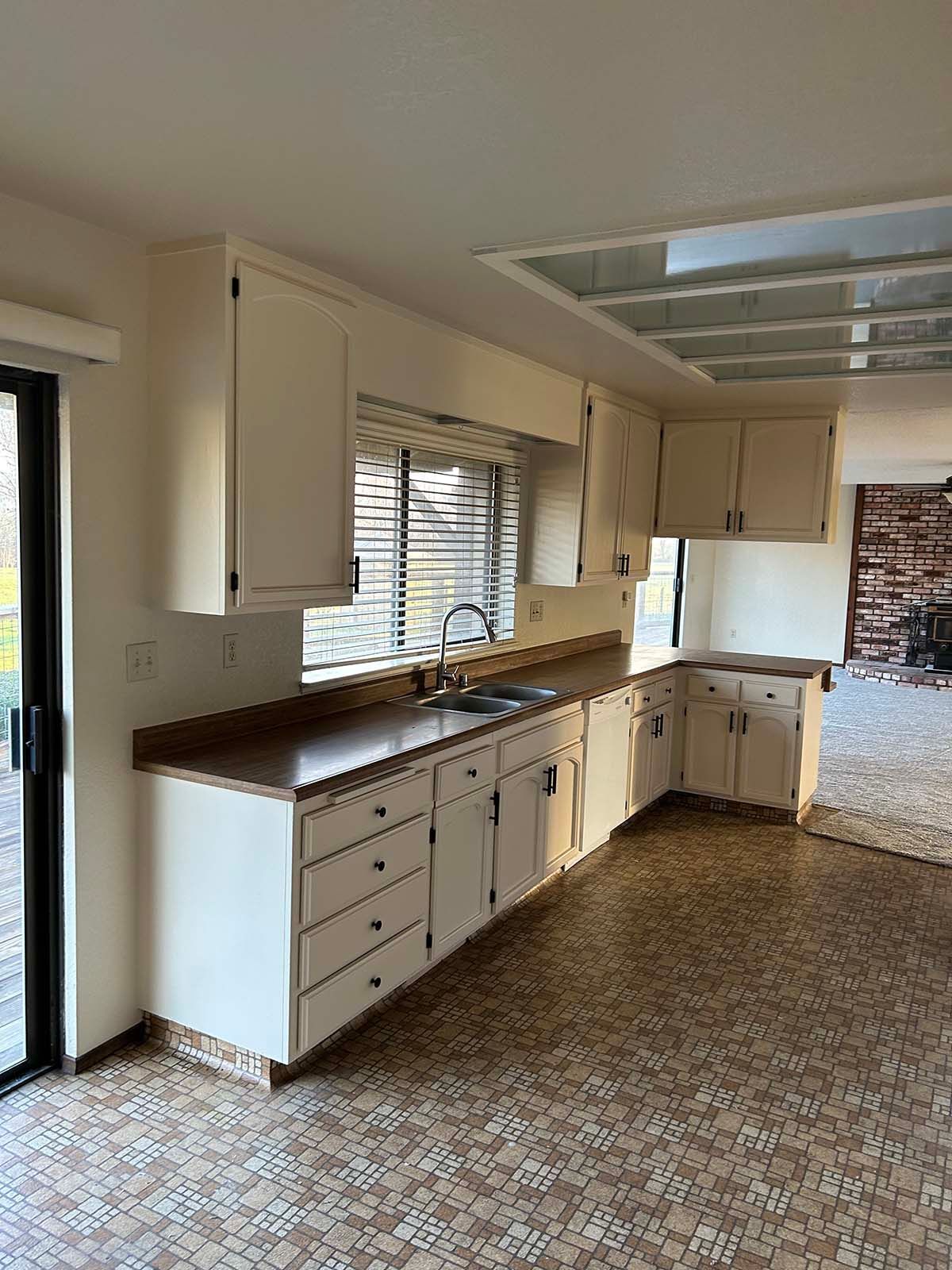 Empty kitchen with white cabinets, wood countertops, patterned flooring, and a window over the sink.
