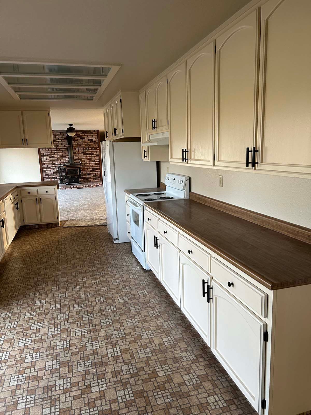 Empty galley kitchen with white cabinets, brown countertops, and patterned tile flooring.