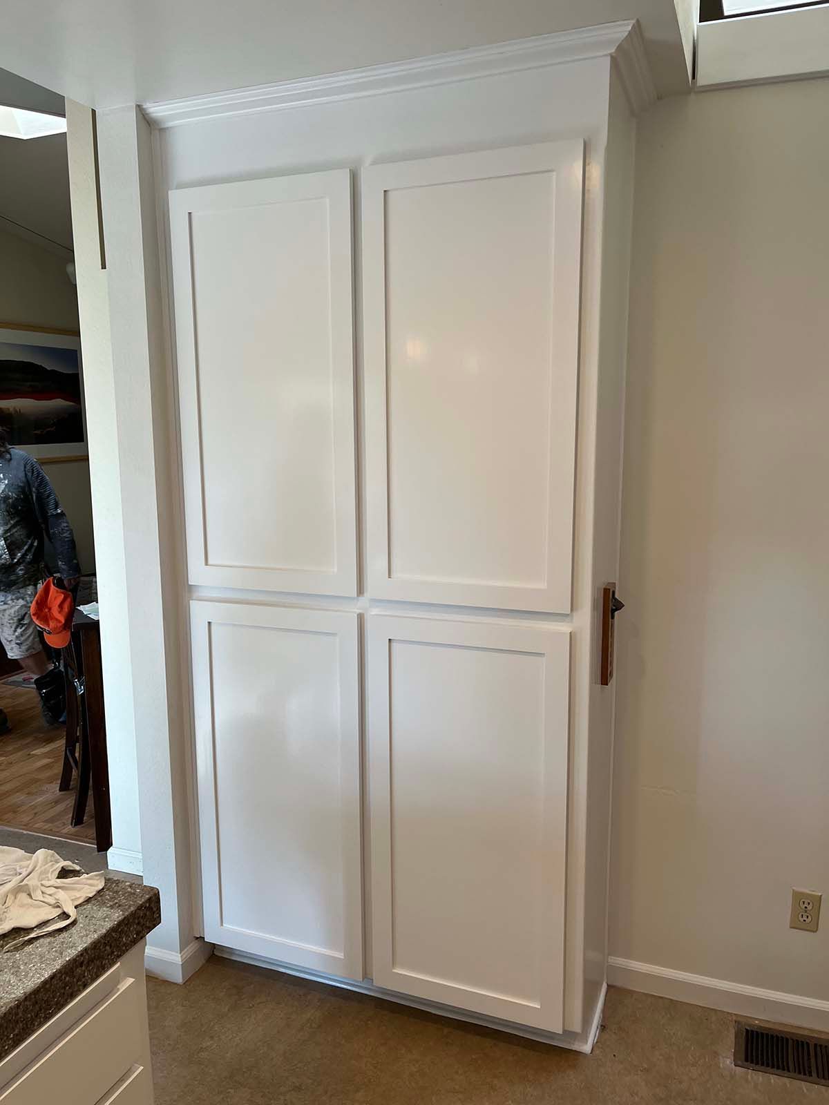White built-in cabinet in a hallway next to a kitchen, with four paneled doors and crown molding