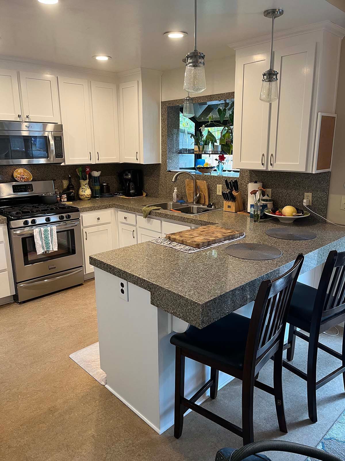 Bright kitchen with white cabinets, stainless steel stove, and a granite island with two chairs