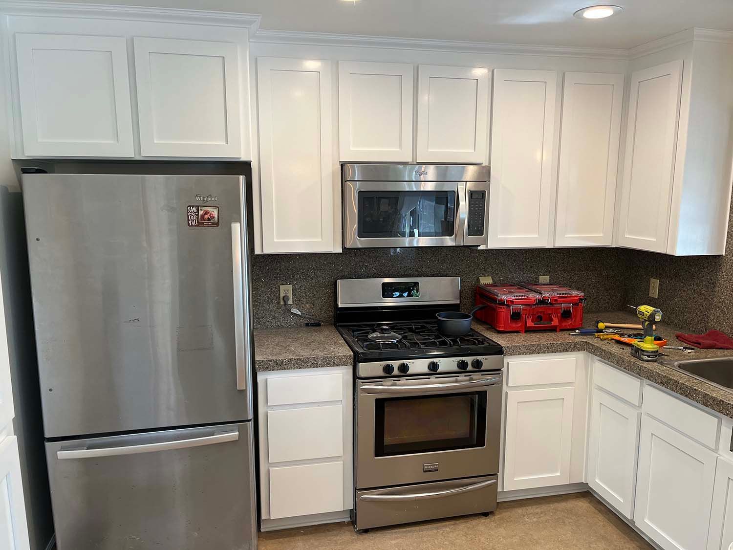 Bright white kitchen with stainless steel appliances, dark countertops, and red cookware on the stove.