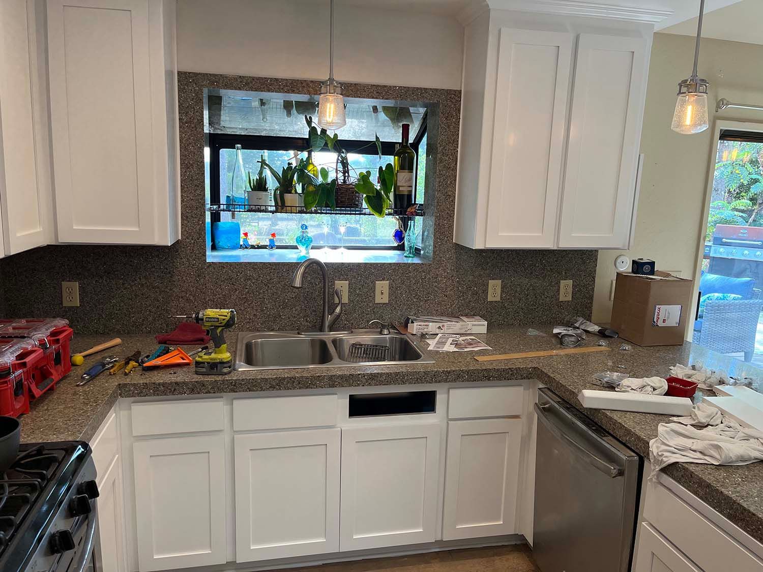 White kitchen with granite counters, stainless sink and dishwasher, and a window over the sink.