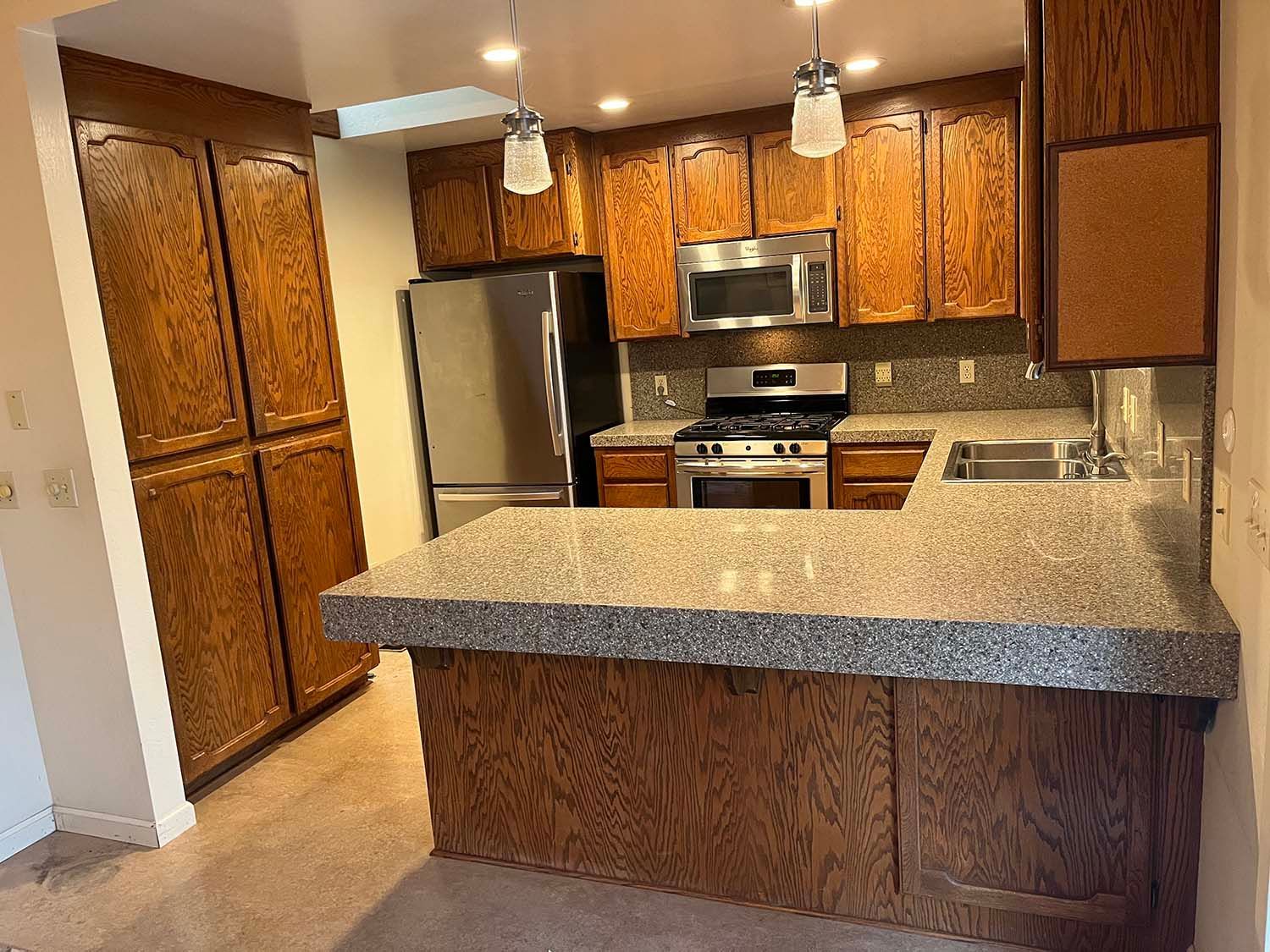 Kitchen with wood cabinets, stainless steel appliances, and a speckled granite island counter.