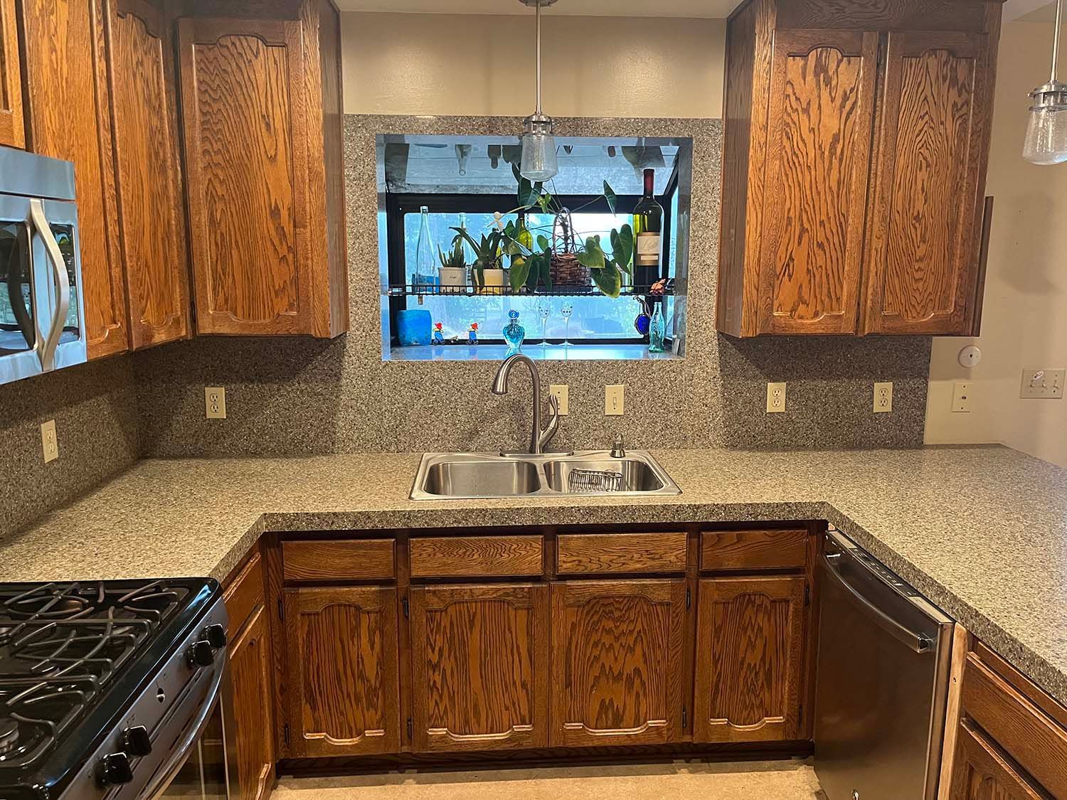 Kitchen with brown wood cabinets, speckled granite counters, stainless sink, and a window over the sink.