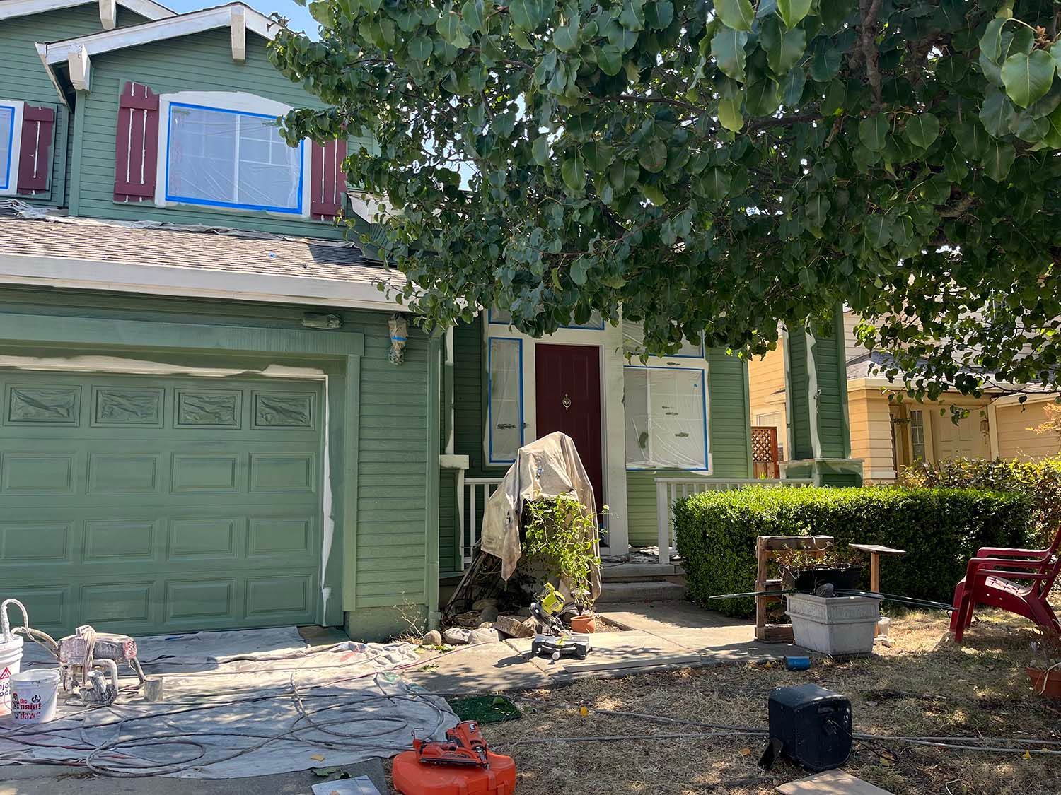 Green two-story house with garage, open front door, and debris scattered across the front yard.
