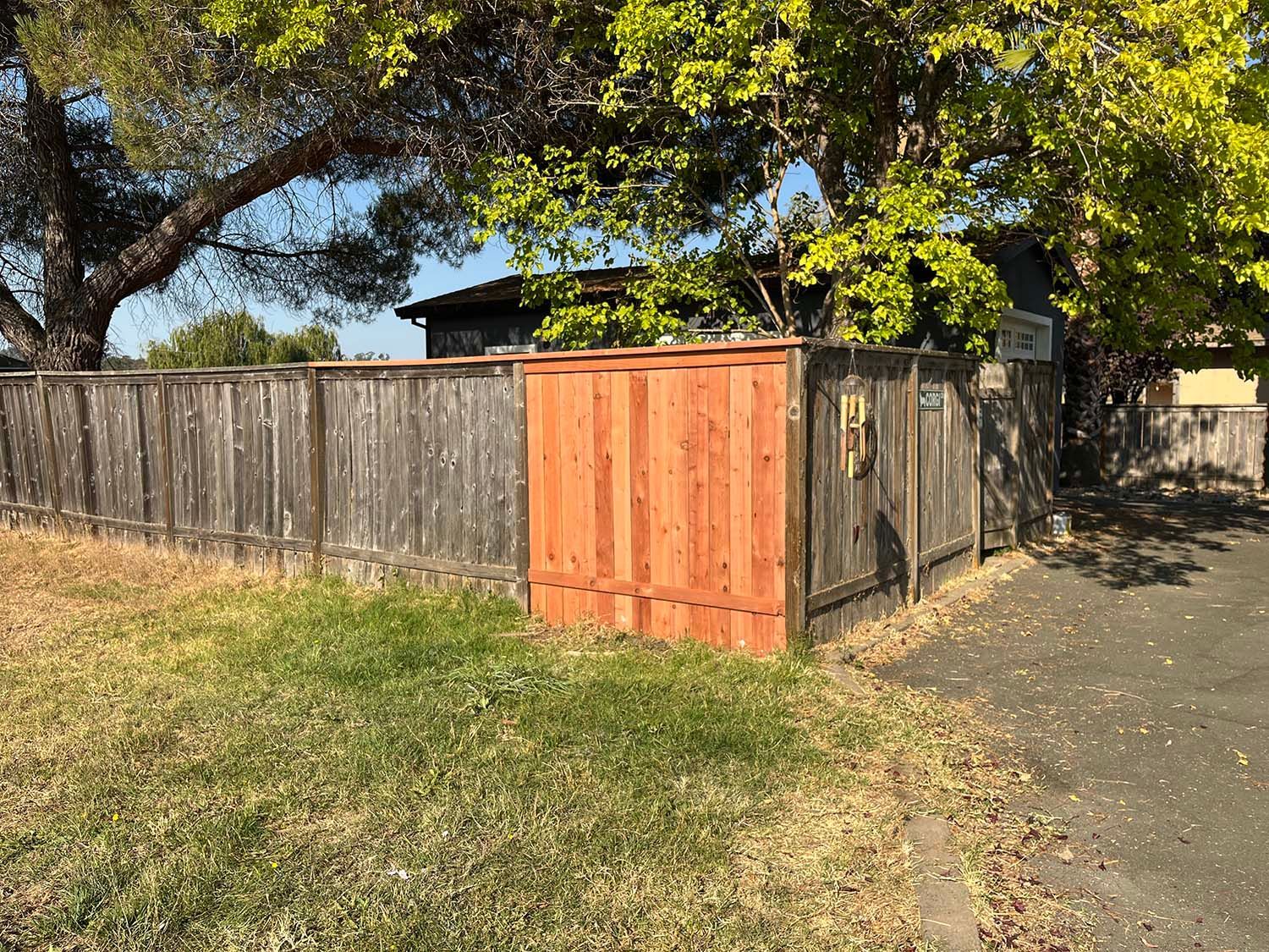 Weathered wooden fence with a bright orange gate beside a dirt path and grassy yard under trees