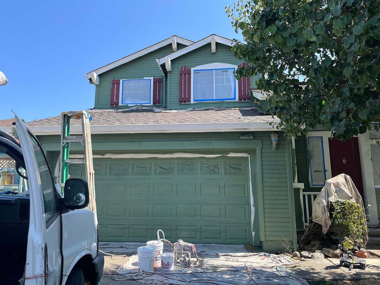 Two-story house with green garage and shutters, viewed from a driveway with a white van on the left.