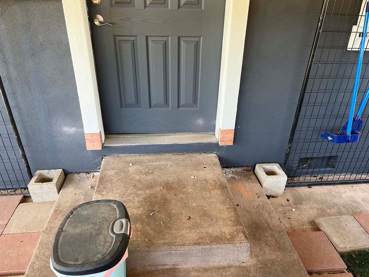Front porch with a gray front door, concrete steps, pavers, and a red-and-black outdoor trash bin in the foreground