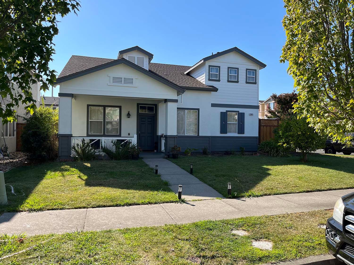 Suburban white house with a front lawn, walkway, and parked car at the curb