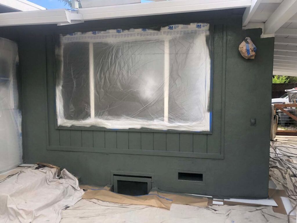 Green house exterior with a window covered in plastic sheeting and drop cloths below