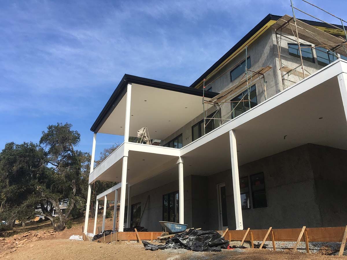 Modern house under construction with white balconies on a dirt lot under a clear blue sky