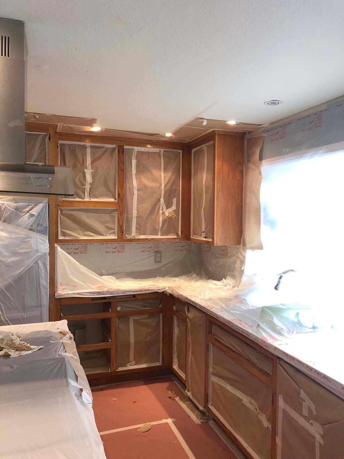 Partially renovated kitchen with taped cabinets, covered countertops, and a bright window over the sink.