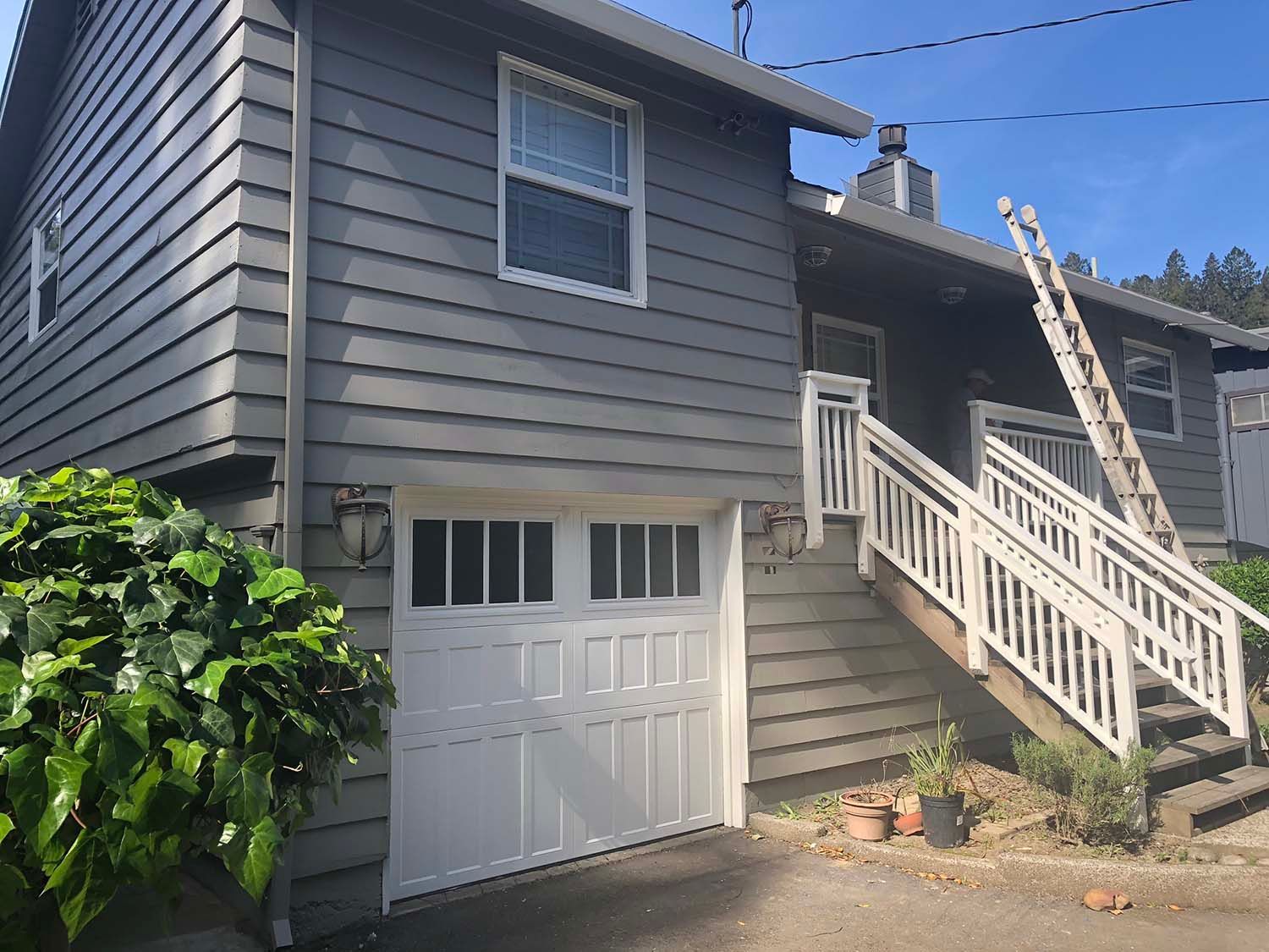 Gray house exterior with white garage door and stairway leading to the upper entrance