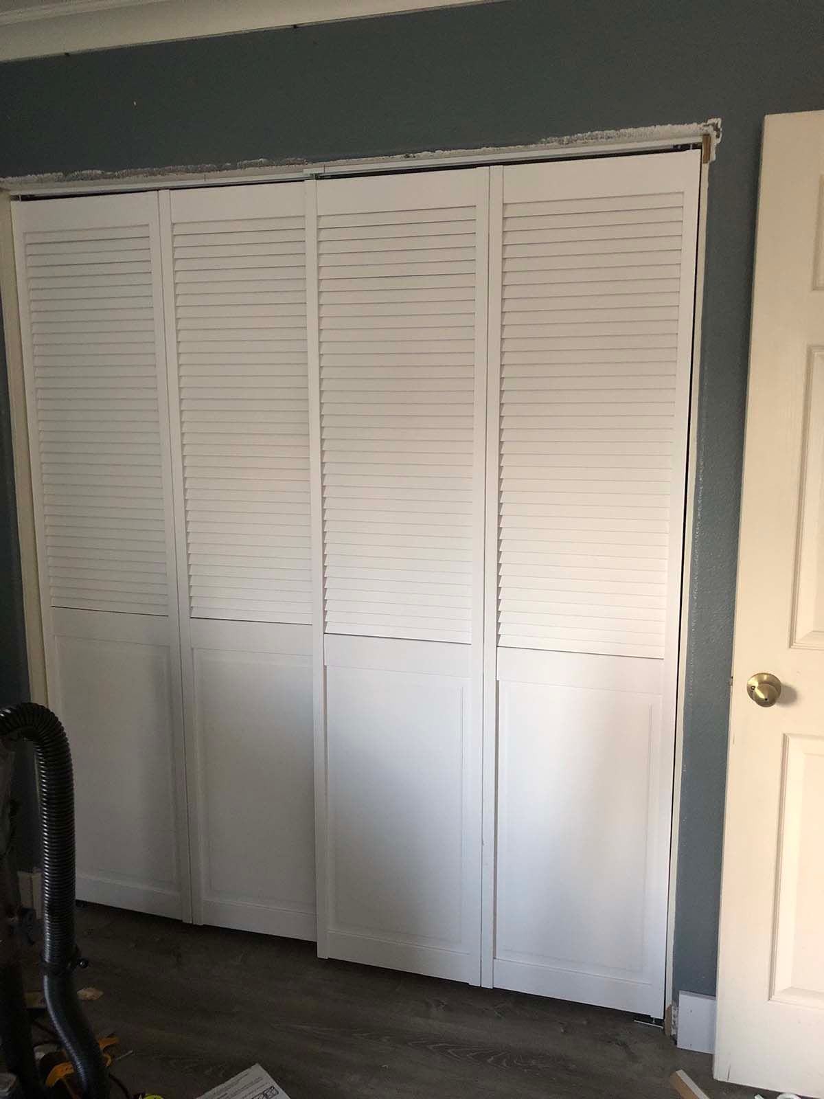White louvered closet doors in a bedroom beside a cream door and dark floor.