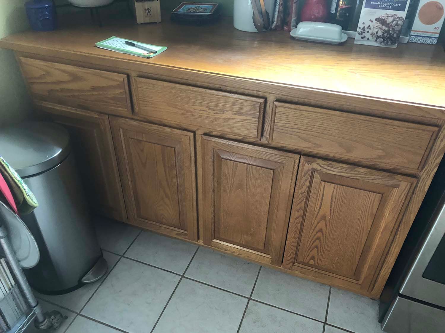 Wooden kitchen cabinets with a trash can and tiled floor beside a countertop