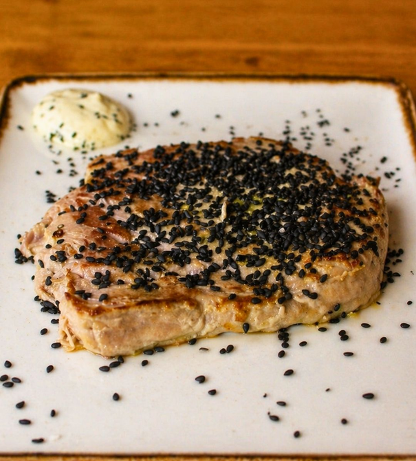 Bife de atum selado com sementes de gergelim preto e uma porção de wasabi em um prato branco.