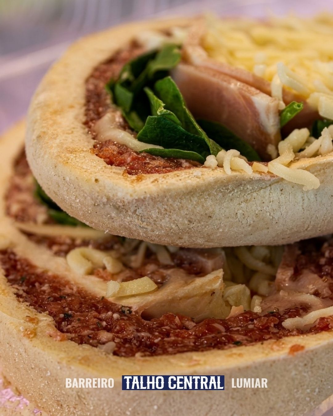 Imagem em close-up de um pão achatado recheado com queijo ralado, verduras e carne, servido em um prato com a marca da empresa.