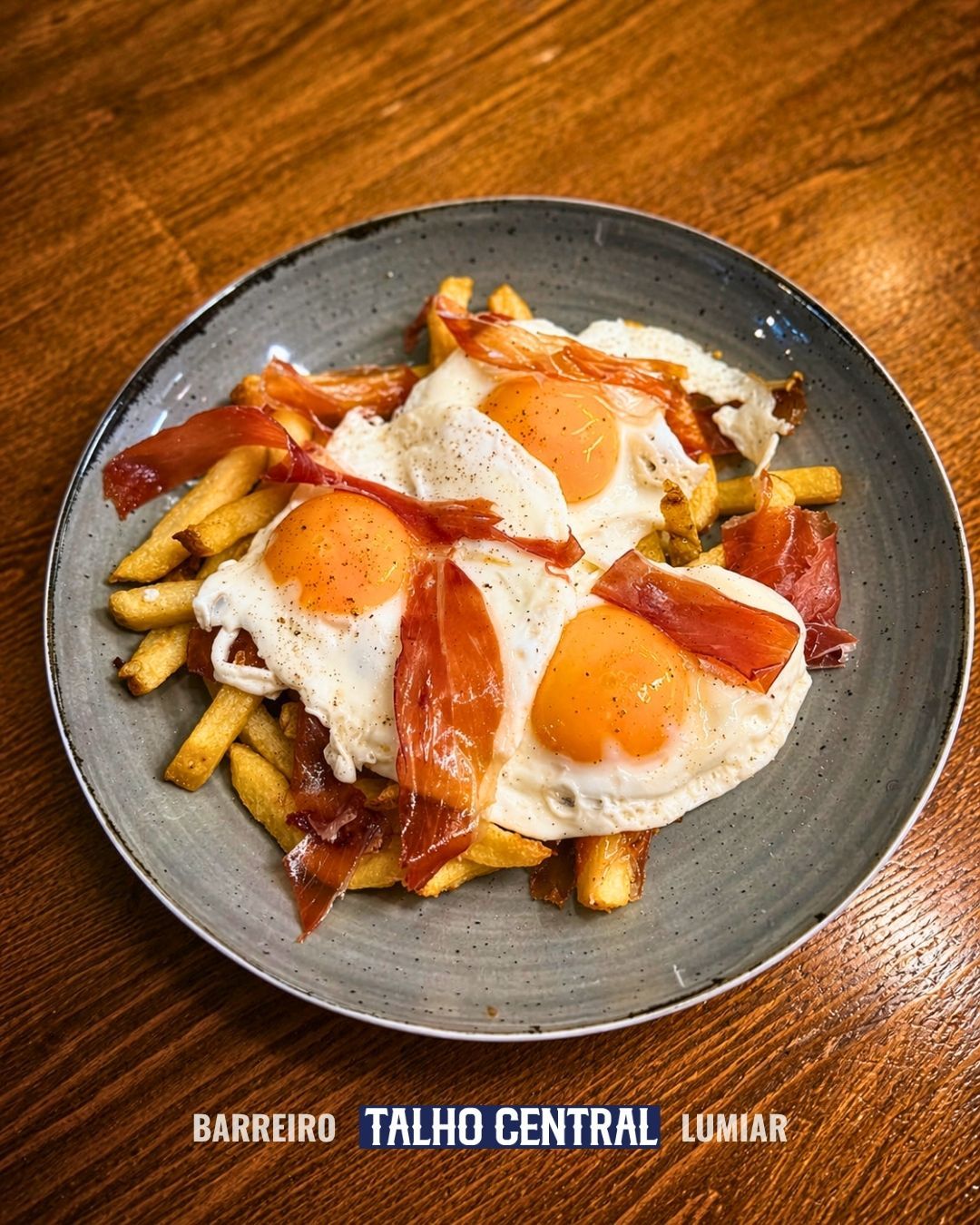 Prato de batatas fritas com ovos fritos, bacon e molho de laranja sobre uma mesa de madeira.