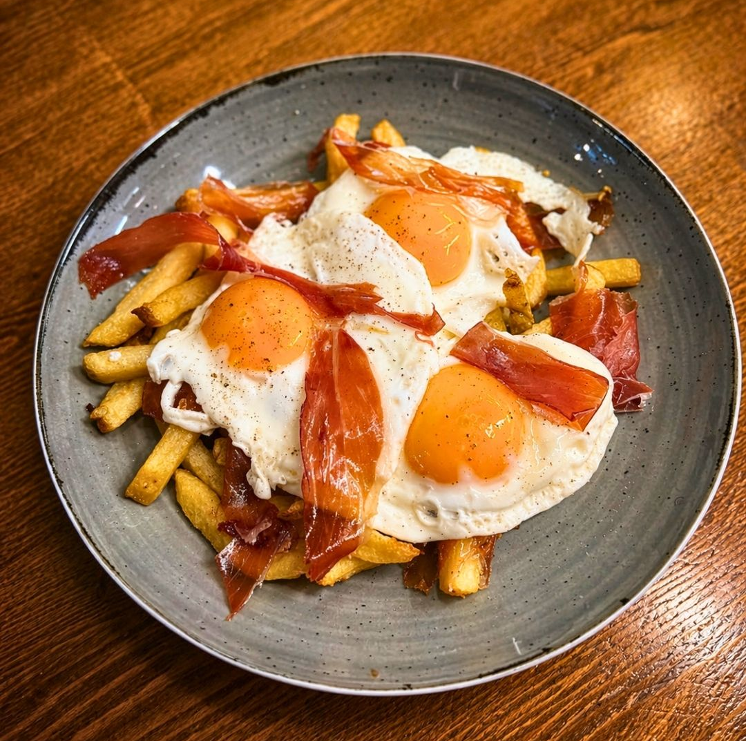 Ovos fritos e presunto sobre batatas fritas em um prato cinza.