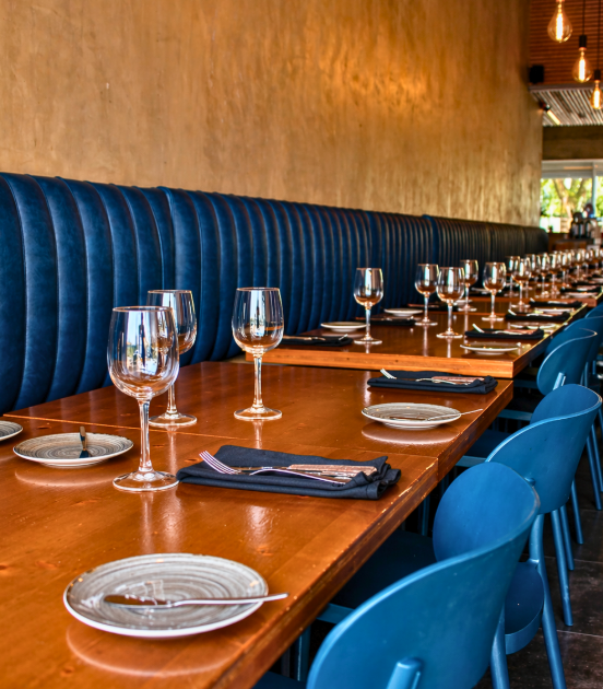 Mesa de jantar comprida de madeira com cadeiras e pratos azuis em um restaurante com iluminação aconchegante.