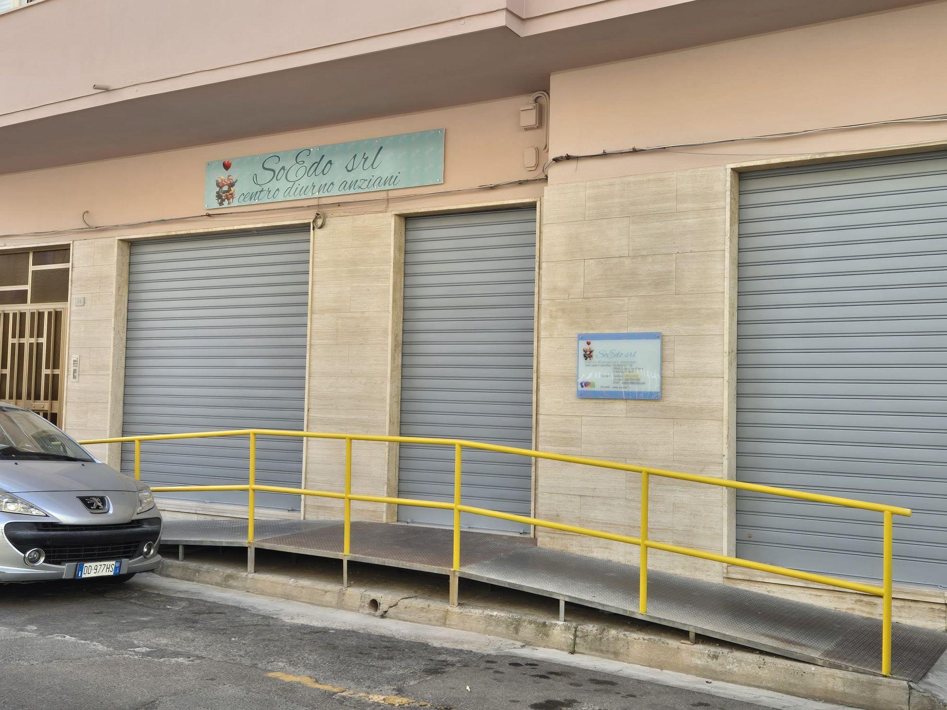 Vetrine chiuse con serrande grigie e una rampa di accesso gialla lungo il marciapiede.