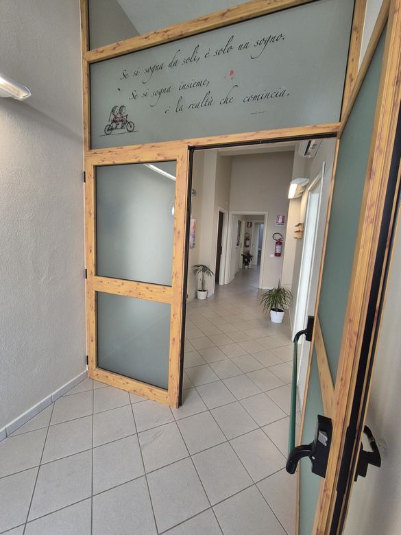 Patio con sedie in vimini nere, porta a vetri e arbusti verdi di fronte a un edificio beige.