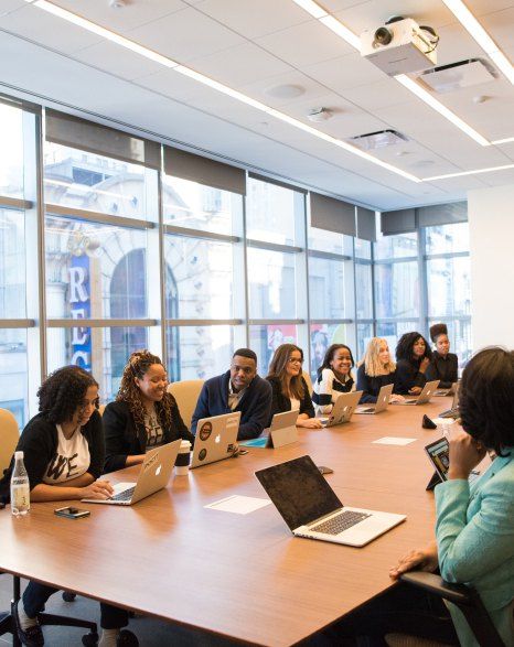 A group of people are sitting around a conference table with laptops.