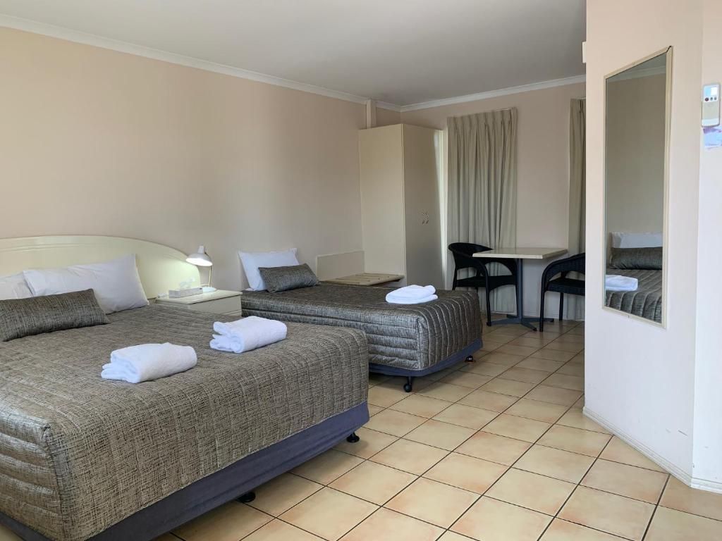 Hotel room with two beds, tiled floor, and a small dining table by the window.