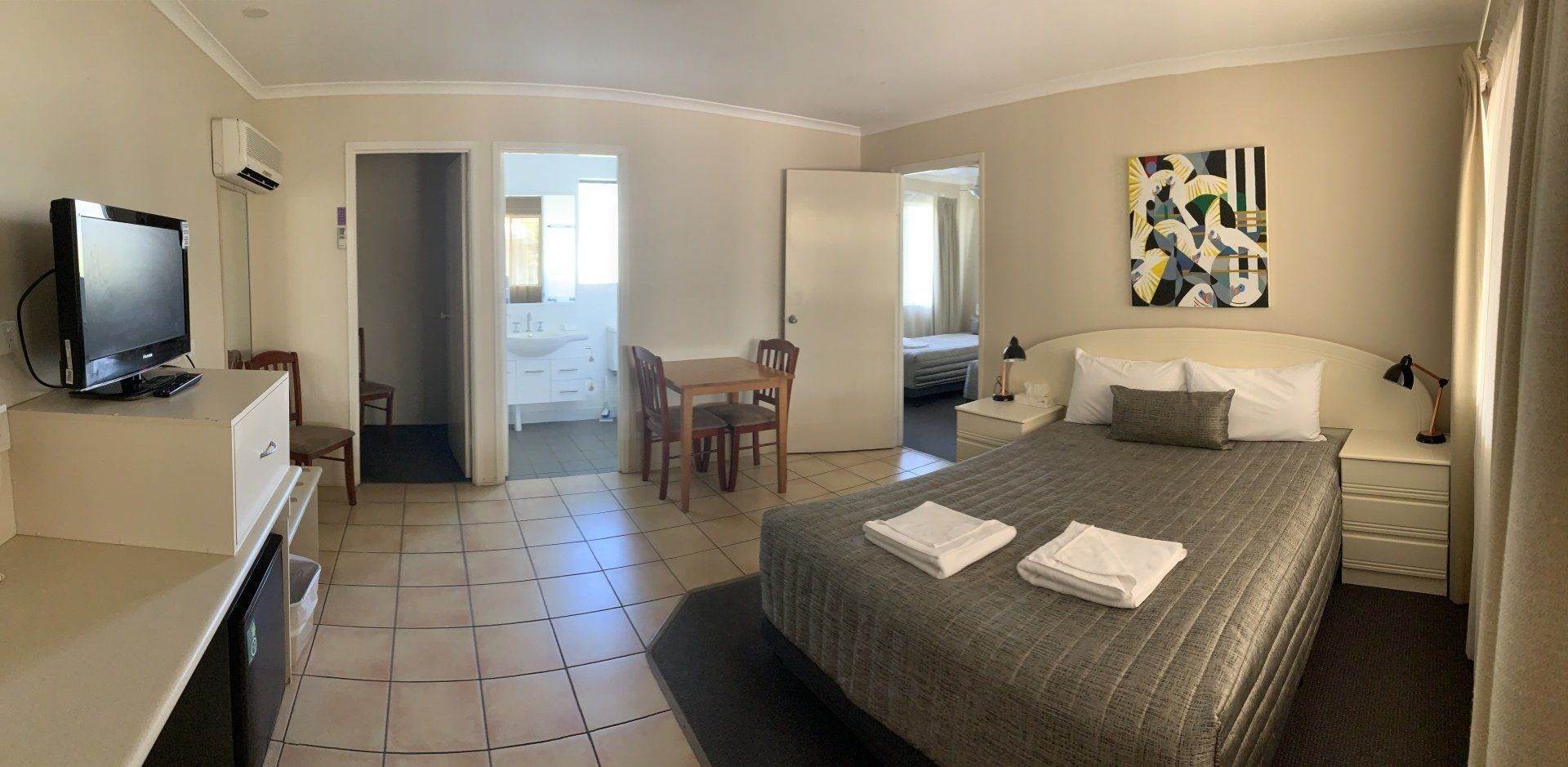 Hotel room with two beds, TV, dining table, and sliding door to balcony with ocean view