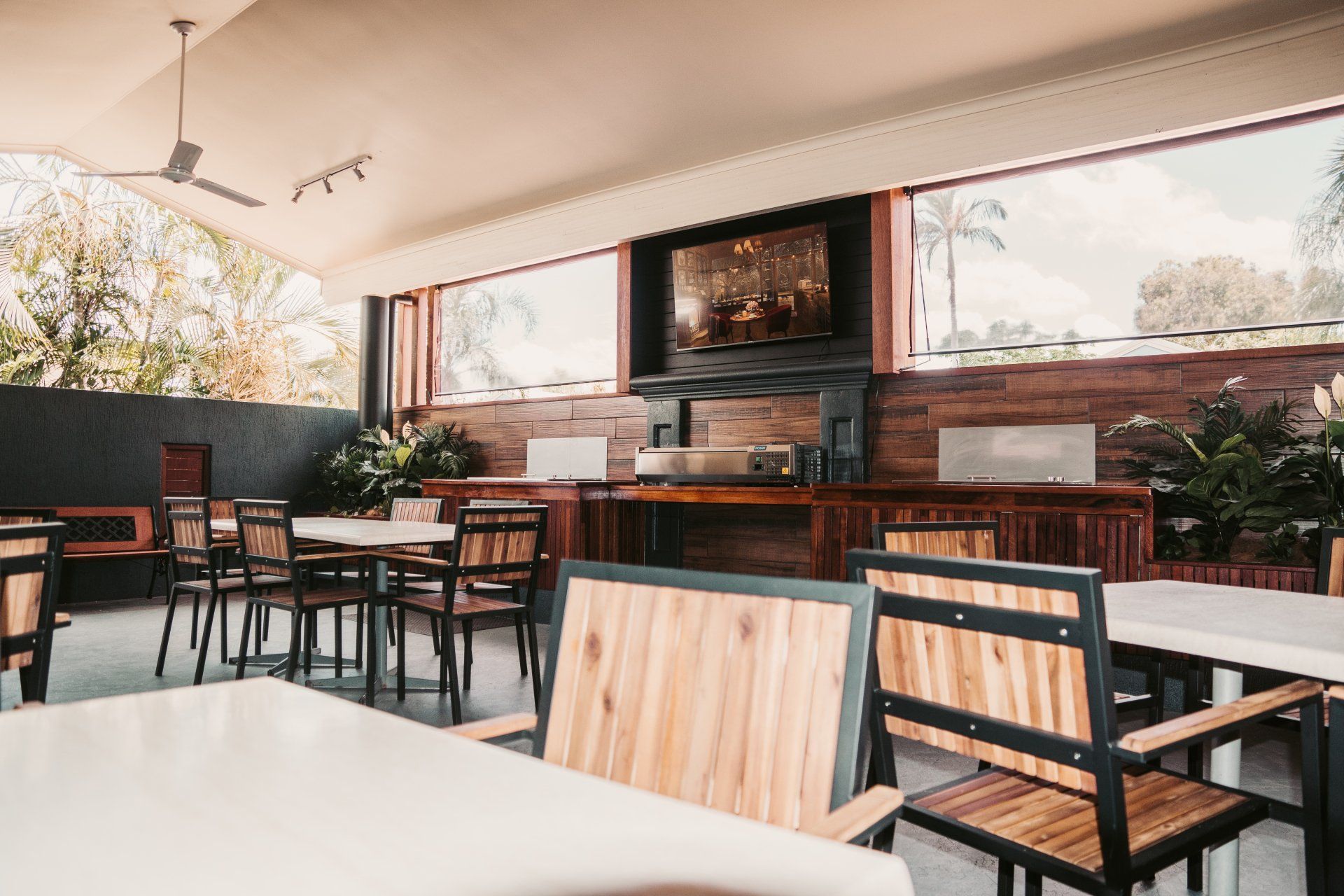 Empty outdoor café seating with white tables, black chairs, and brick wall decor under a covered patio