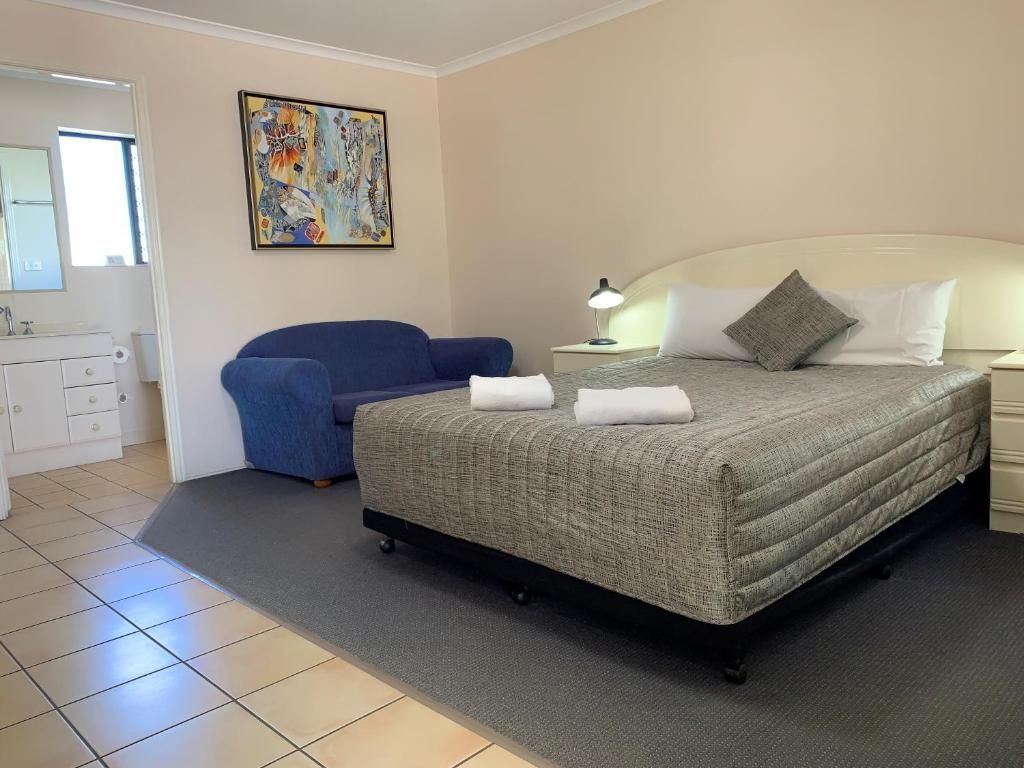Bedroom with a bed, blue chair, tiled floor, and framed abstract artwork.
